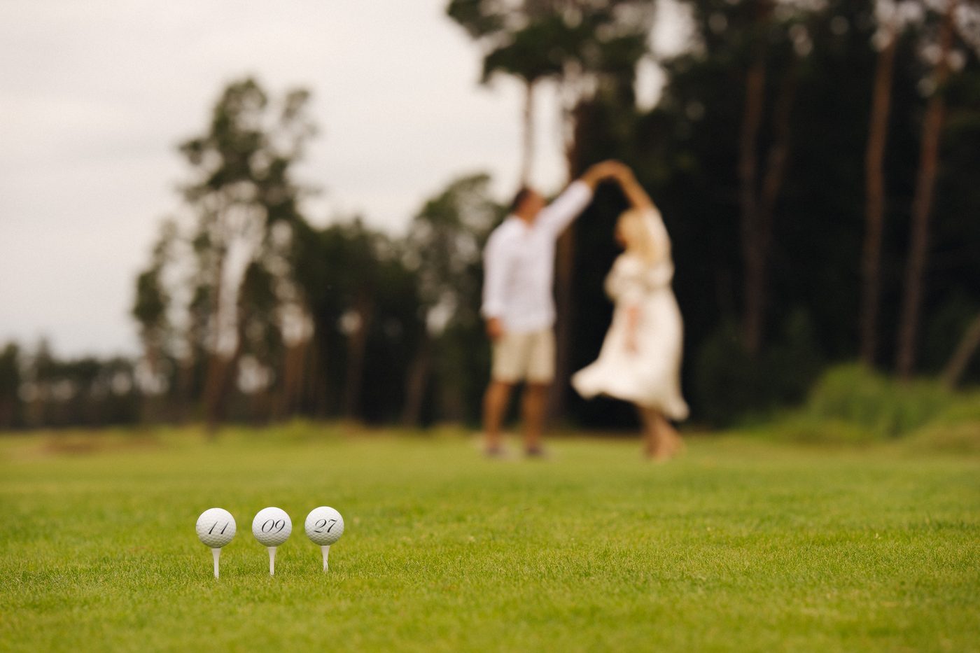 Kaja ja Arto tantsivad golfiväljakul, esiplaanil kolm golfipalli numbritega 11, 09 ja 27